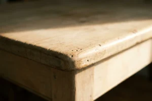 The worn edge of a pale oak table lit from the right